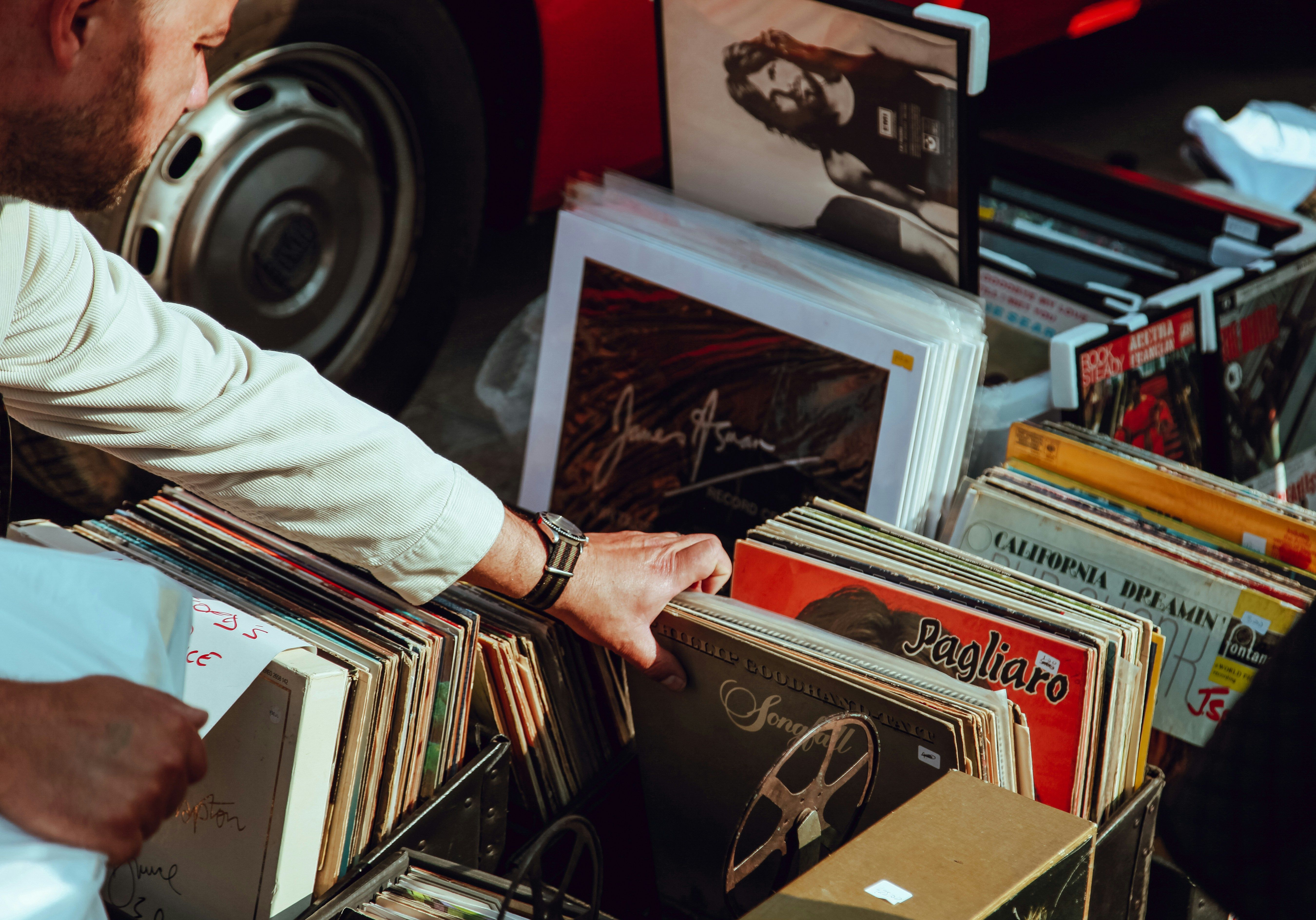 A man flipping through crates of used vinyl records at an outdoor record fair, album sleeves packed tight in the bins.