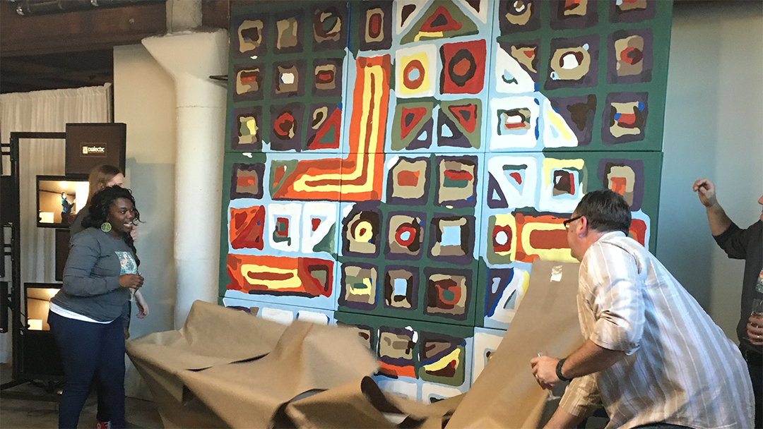 Guests at the launch party pulling brown kraft paper off a wall-sized painted mural of the Dialectic 'D,' its grid of colored cells revealed beneath, at the Dialectic offices.