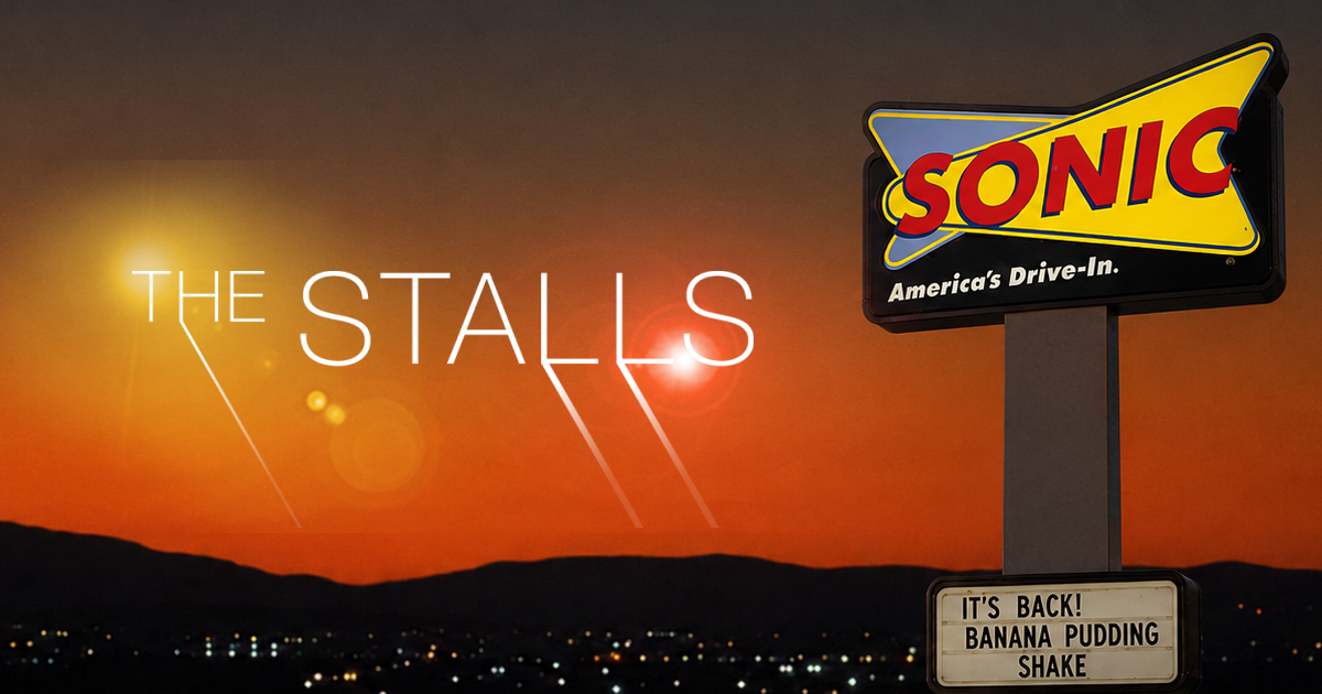 The Stalls homepage: a dark cosmic starfield header with 'THE STALLS' in thin serif caps and a Sonic drive-in at dusk on the right, a left nav, a trailer pane over a nebula, and a three-column grid of Full Episodes, Latest Updates, and What's In/Out.